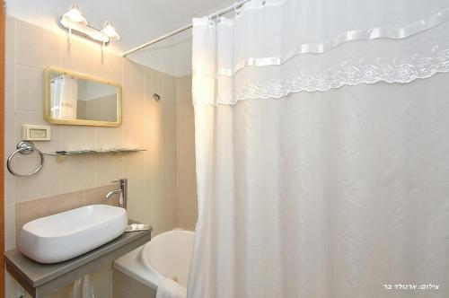 a bathroom with a white shower curtain and a sink at אחוזת הוואי in Had Nes