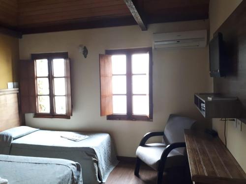 a room with two beds and a chair and two windows at Pousada Raio de Sol in Jaguarão