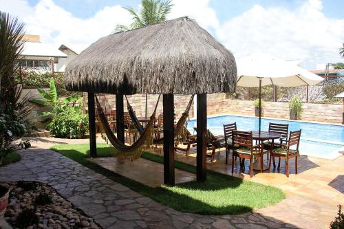 a table and chairs under a straw umbrella next to a pool at Pousada do Galo in Porto De Galinhas