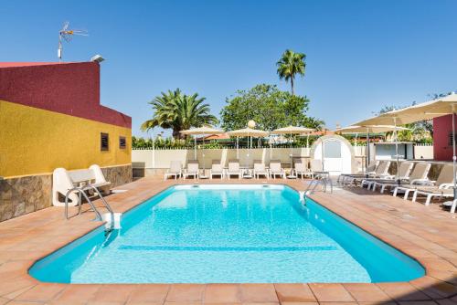 una piscina en un hotel con sillas y sombrillas en Bungalow Villa Golf Maspalomas, en Maspalomas