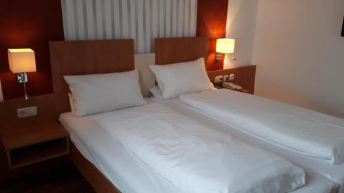 Gasthof Sommer في Bösel: سريرين في غرفة الفندق مع شراشف ووسائد بيضاء