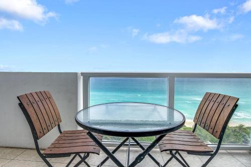 a glass table and two chairs on a balcony with the ocean at Castle 828 Oceanfront view with balcony, pool, tennis, beach access and free parking! in Miami Beach