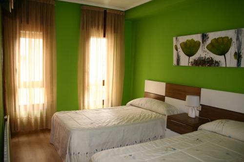 a green bedroom with two beds and two windows at Hotel Restaurante Valdevenados in Anguiano