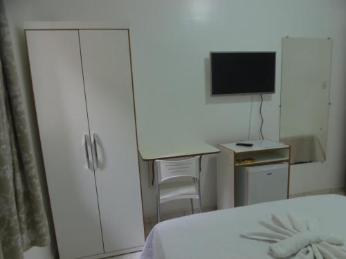 a bedroom with a bed and a desk with a television at Hotel Miranelli in Barbacena