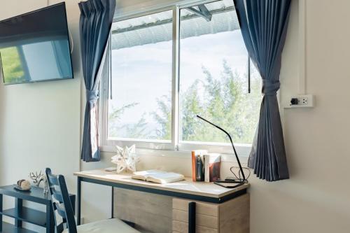 a desk in front of a window with blue curtains at THE BEACH CHA AM Suites in Cha Am