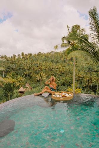 a woman sitting on a raft next to a swimming pool at Adiwana Dara Ayu Villas in Payangan
