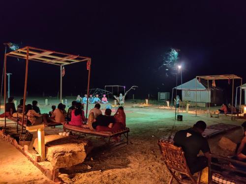 un grupo de personas sentadas en sillas en una playa por la noche en Savi Camps Jaisalmer, en Sām