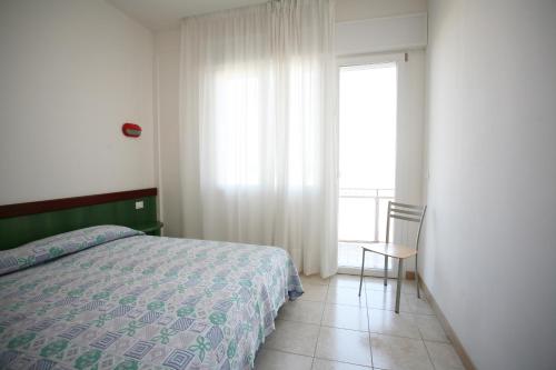 una camera da letto con un letto, una sedia e una finestra di Residence Capinera a Sottomarina