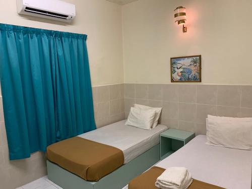two beds in a room with blue curtains at Fairway Hotel in Malacca