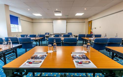 a conference room with tables and chairs and a screen at Britannia Hotel Wigan in Standish