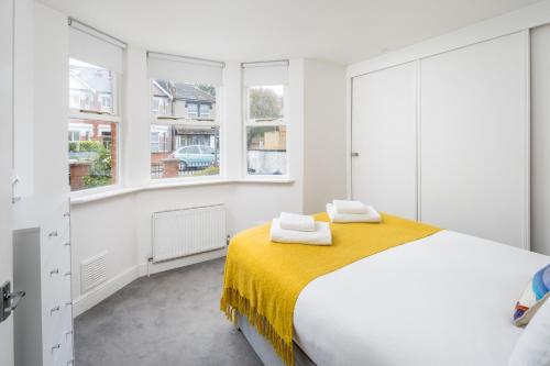 Stunning 2-bed flat w/ garden patio in West London في لندن: غرفة نوم بيضاء بها سرير ونوافذ