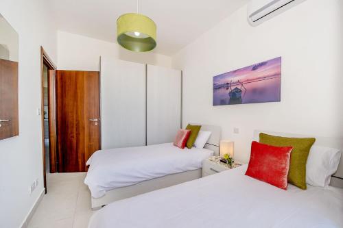 two beds in a room with white sheets and red pillows at Hillock Residence Apartments in Marsalforn