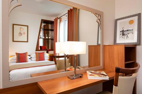a bedroom with a bed and a desk with a mirror at Grand Hotel des Balcons in Paris