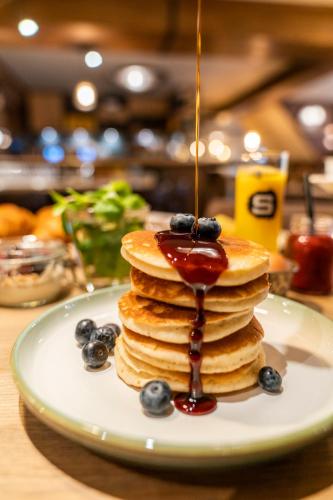 a stack of pancakes with syrup and blueberries on a plate at Boutique Hotel De Smulpot in Den Burg