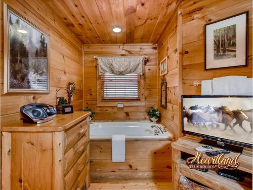 a log cabin bathroom with a tub and a tv at Naughty Pines in Pigeon Forge