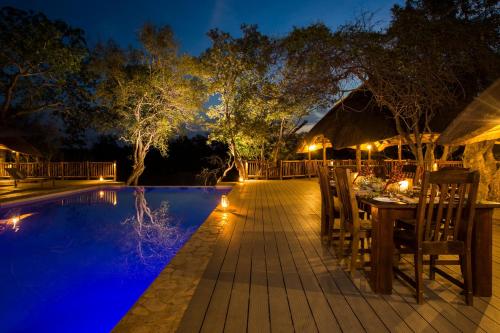 a table and chairs next to a pool at night at Vuyani River Lodge in Hoedspruit
