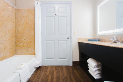 een badkamer met een witte deur, een wastafel en een bad bij Palacio Royale Inn Signature Katy in Katy