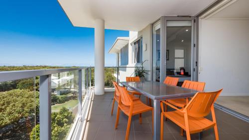 a dining room with orange chairs and a table on a balcony at White Shells Luxury Apartments Marcoola in Marcoola