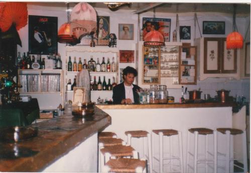 un hombre sentado en un bar en un restaurante en Manos STUDIOS & APARTMENTS en Skopelos Town