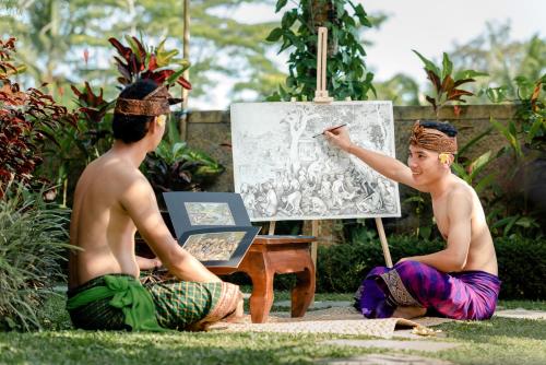 two men sitting on the grass painting a picture at Cenik Villa Ubud in Ubud