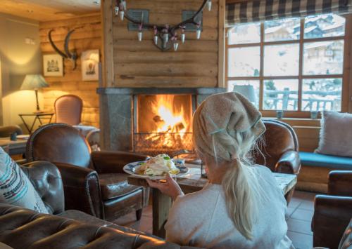 a woman holding a plate of food in front of a fireplace at Hamilton Lodge & Spa in Belalp