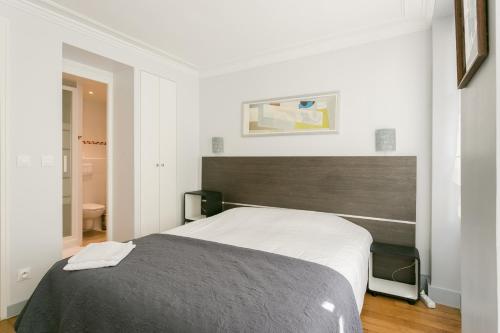 une chambre avec un grand lit dans une pièce blanche dans l'établissement Sourdiere Louvre Vendome with AC, à Paris