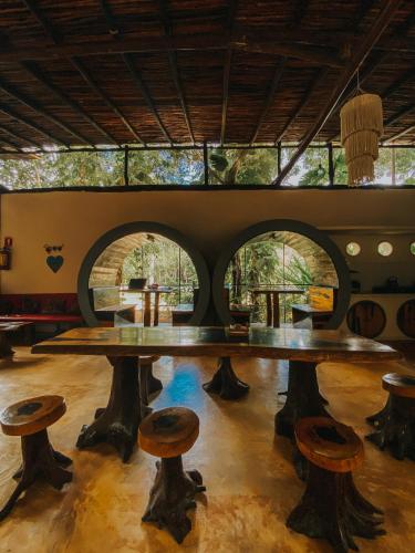 una mesa grande y taburetes en una habitación con ventanas en Tubo Tulum Hostel, en Tulum