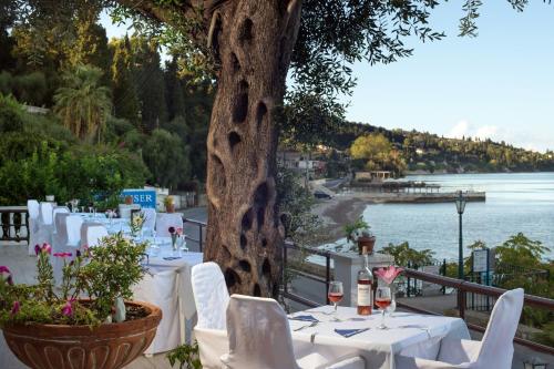 a table with white tables and chairs under a tree at Hotel Kaiser Bridge in Benitses