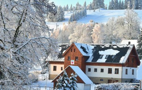 a building covered in snow with trees and a mountain at Penzion Jizerská Malina in Bedřichov