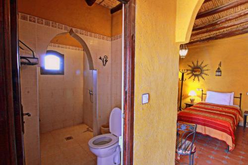 a bathroom with a toilet and a shower and a bed at Riad Nezha in Merzouga