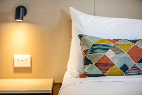 a bed with a pillow and a light on a wall at Nightcap at Sylvania Hotel in Campbellfield