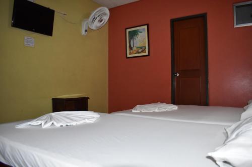 two white beds in a room with orange walls at LA POSADA DEL VIAJERO in Ibagué
