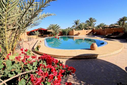 a swimming pool in a resort with red flowers at Riad Nezha in Merzouga