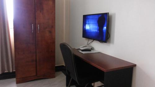 a desk with a computer and a monitor on a wall at Hotel Good News in Lira