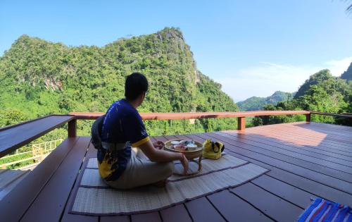 a man sitting on a deck looking at the mountains at ม่านฟ้า โฮมสเตย์ MaanFah Homestay in Chiang Rai