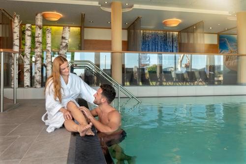 a man and woman sitting next to a swimming pool at Landrefugium Obermüller 4,5 Sterne in Untergriesbach