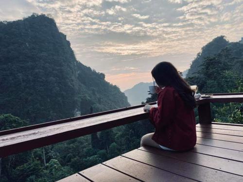 a girl sitting on a wooden deck looking at the mountains at ม่านฟ้า โฮมสเตย์ MaanFah Homestay in Chiang Rai