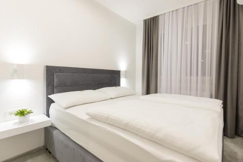 a white bedroom with a large white bed and a window at Apartmani i sobe Pejačević in Osijek