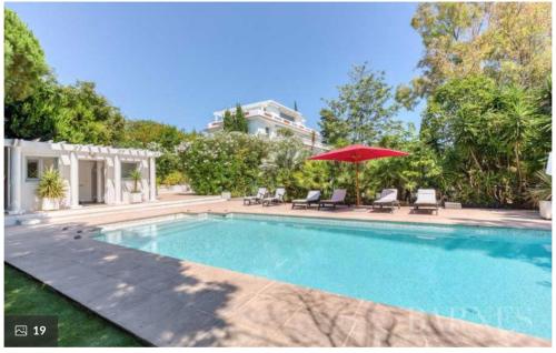 - une piscine avec un parasol rouge et des chaises dans l'établissement The Gatsby Mansion, à Antibes