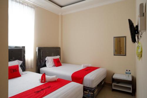 duas camas num quarto com lençóis vermelhos e brancos em RedDoorz near Millenium Waterpark Palu em Palu
