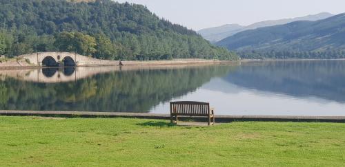 a bench sitting on the grass near a body of water at CREAG DHUBH COUNTRY HOUSE in Inveraray