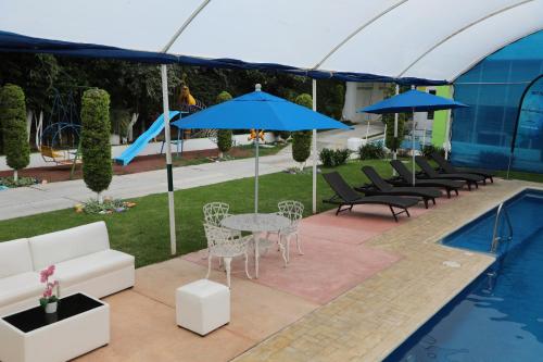 een patio met een tafel, blauwe parasols en een zwembad bij Hotel Maragreens in Tetela del Volcán