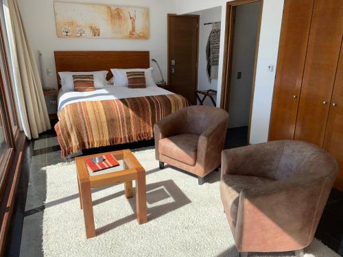 a bedroom with a bed and two chairs and a table at Hotel Playa Grande Suites in Pucón