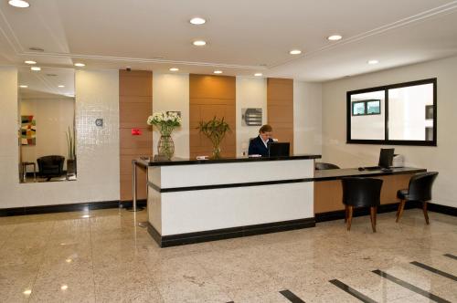 a woman standing at a reception desk in a lobby at Hotel Domani in Guarulhos