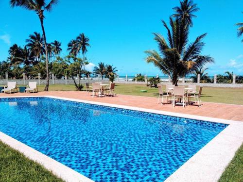 a swimming pool with chairs and palm trees and the ocean at APARTAMENTO À BEIRA MAR - PÉ NA AREIA - Ilhéus in Ilhéus