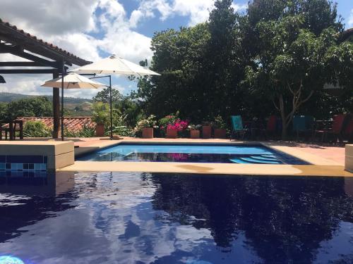 a swimming pool with an umbrella and some trees at Achiotte by Masaya Collection in Barichara