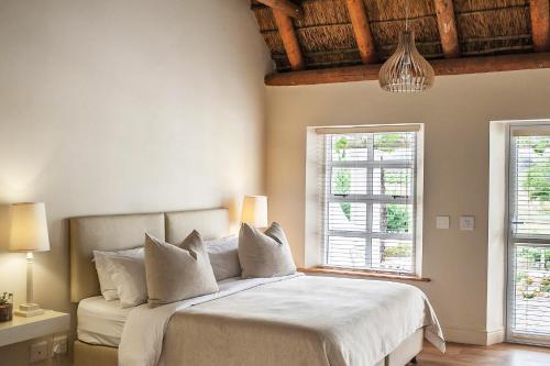 a bedroom with a bed with white sheets and two windows at Rijk's Guesthouse in Tulbagh