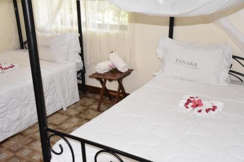 two beds in a room with white sheets and flowers at Fanaka Safaris Campsite & Lodges in Mto wa Mbu