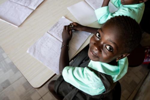 a young girl sitting at a table with a book at Tamba Kuruba Eco-lodge in Folonko