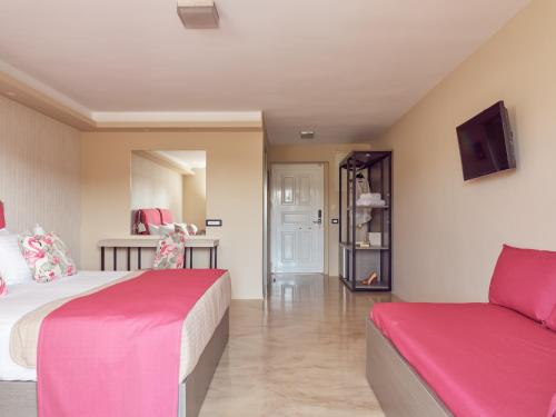 a bedroom with two beds with pink sheets and a tv at Koukounaria Hotel & Suites in Alykes